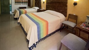 Une chambre d’hôtel avec deux lits, une tête de lit en bois, une chaise, une petite table et une lampe fixée au mur.