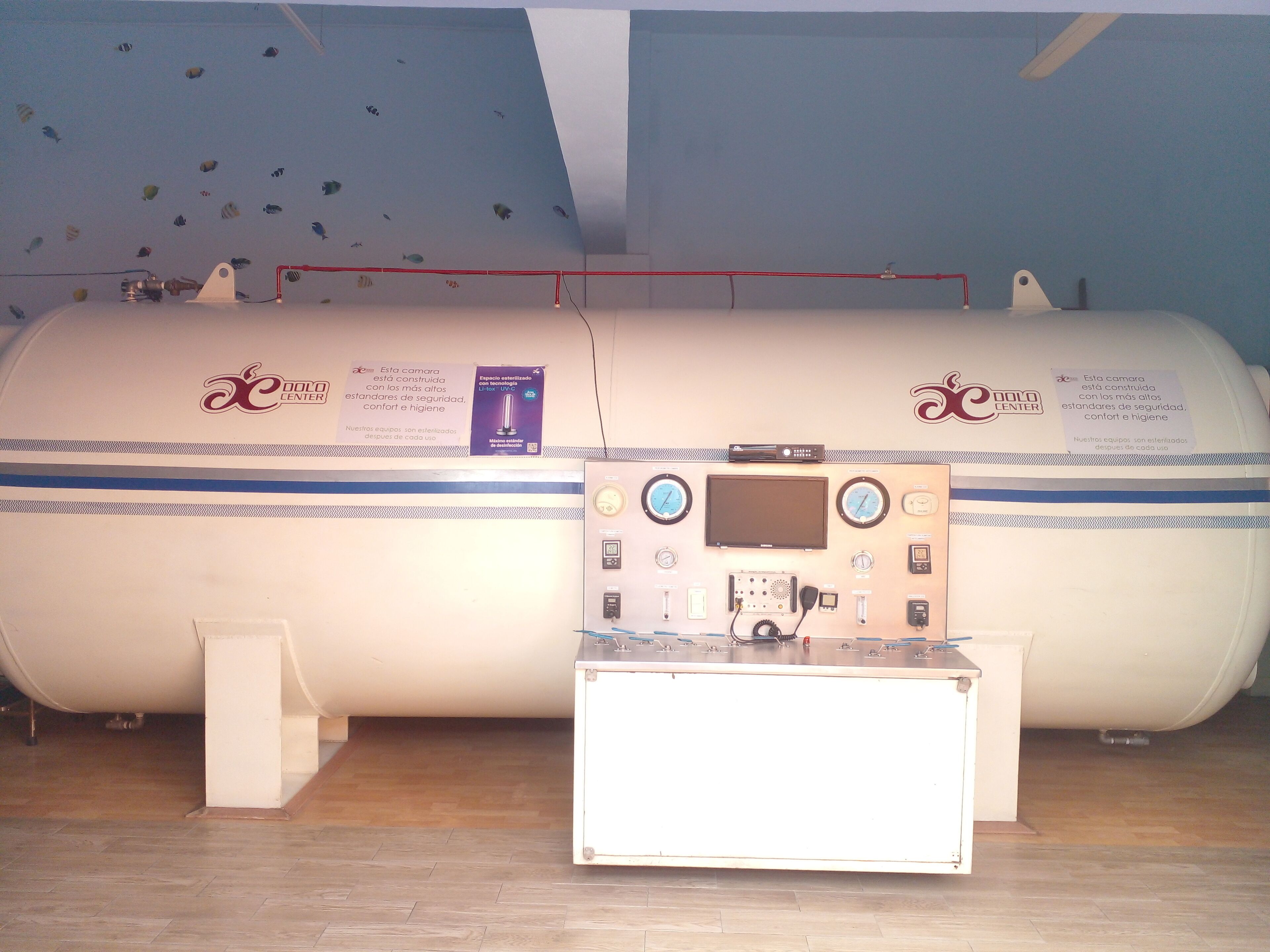 Una sala per esami diagnostici con due grandi macchinari cilindrici, un pannello di controllo e un piccolo tavolo bianco.