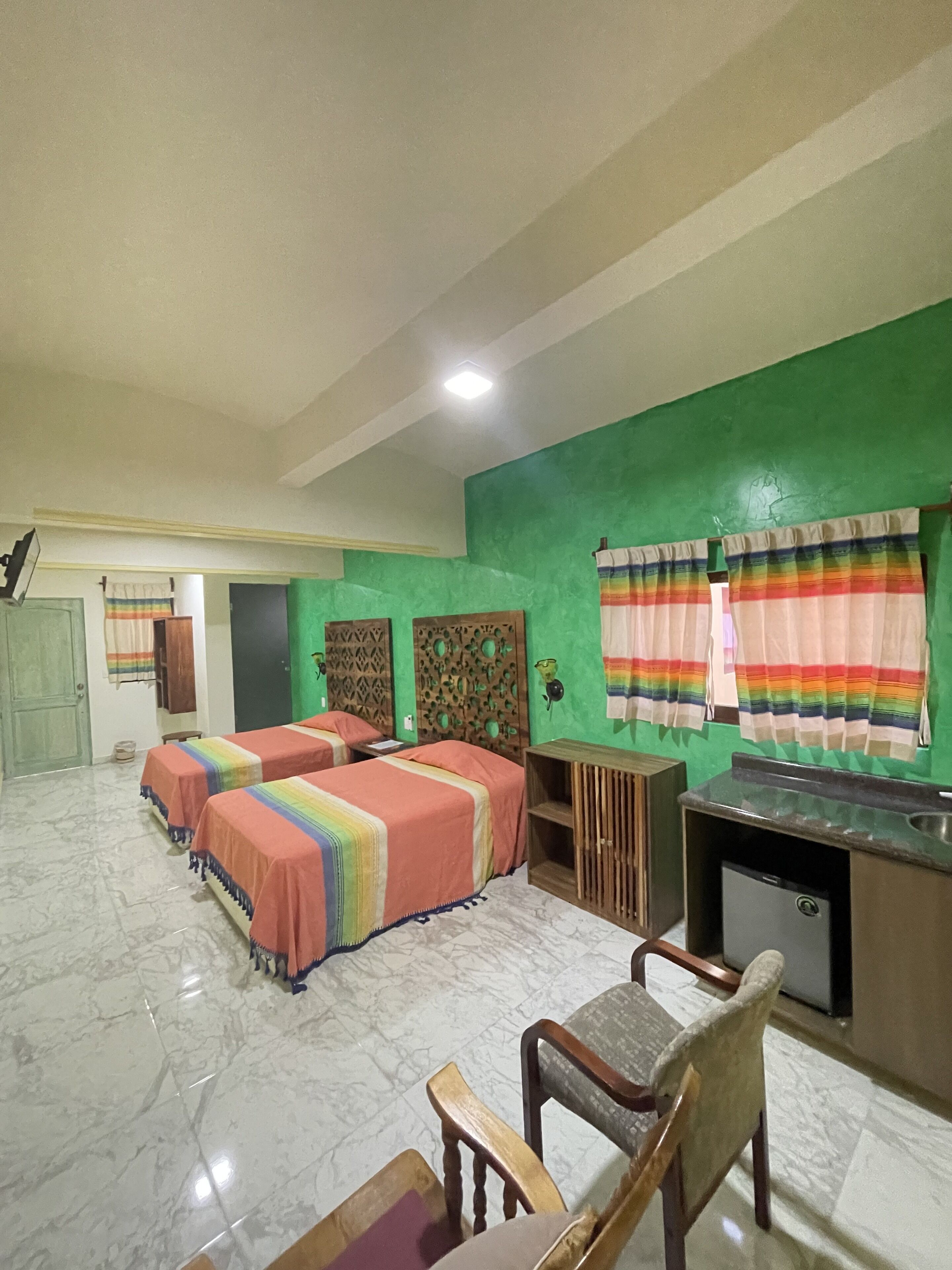 Habitación de hotel con dos camas, un escritorio, una silla y una kitchenette pequeña.