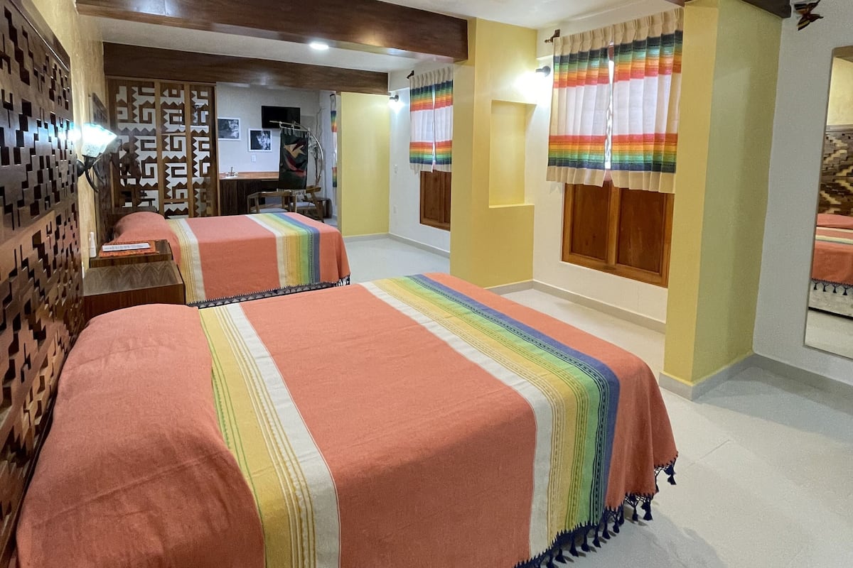 A hotel room with two beds, a wooden headboard, a small table, and a wall-mounted TV.