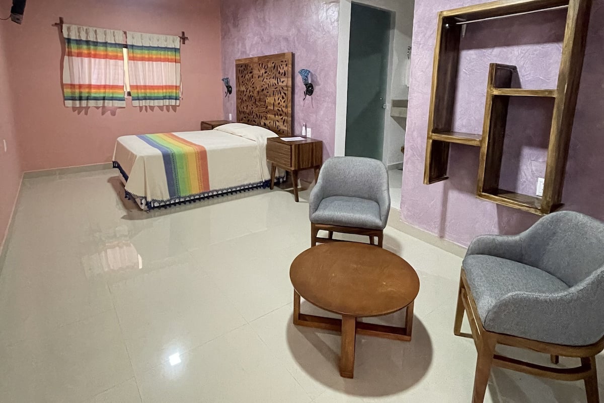 A spacious room with a bed, two armchairs, a small wooden table, and a decorative headboard.