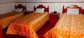 A hotel room with three single beds, each with a wooden headboard and a floral-patterned bedspread. There is a small wooden nightstand with a telephone on it. - HOSTAL MONARCA (Cusco)