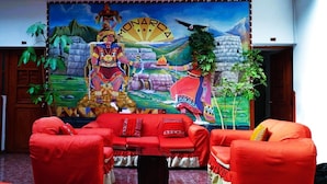 A room with red sofas, a mural depicting a cultural scene, and a small table. - HOSTAL MONARCA (Cusco)