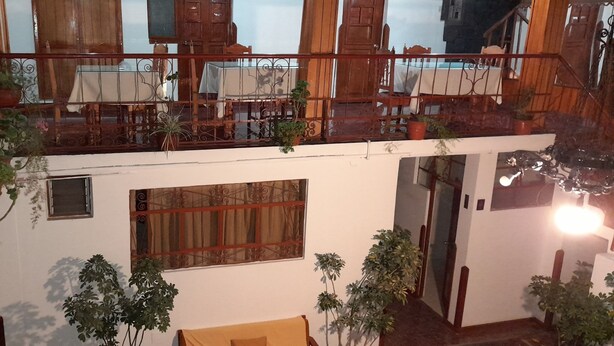 A multi-level wooden balcony with potted plants, a dining area with tables and chairs, and a small window with curtains. - HOSTAL MONARCA (Cusco)