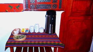 A table with a colorful tablecloth, a thermos, a basket of food, and several bottles and containers. - HOSTAL MONARCA (Cusco)