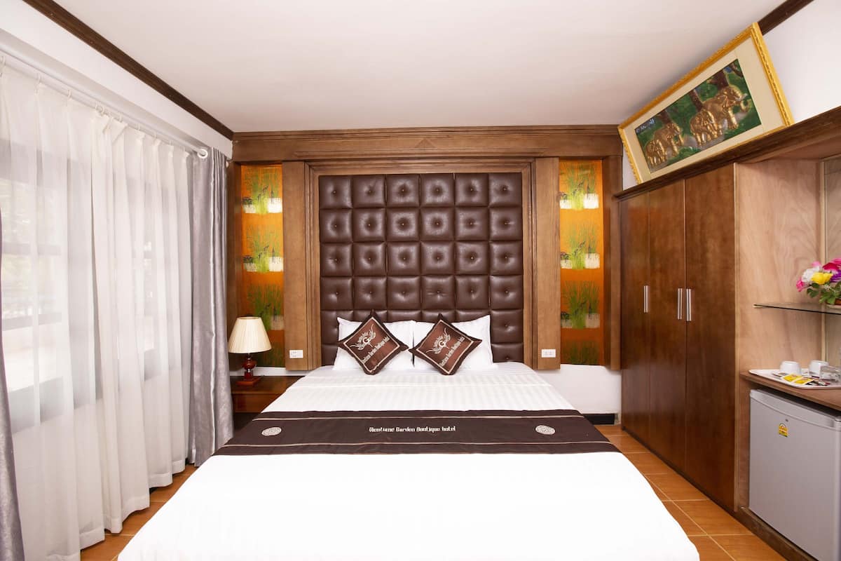 A hotel room with a large bed, a wooden headboard, a nightstand with a lamp, and a wardrobe.