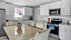 A modern kitchen with white cabinets, a stainless steel refrigerator, a microwave, an oven, and a dining table with chairs. - 🏖 Beautiful Bay View Condo “Close To Beach” 🏖 (Ventnor City)