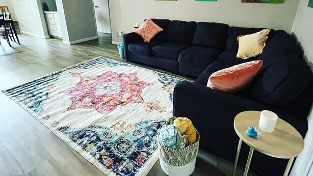 Olohuoneessa on tummansininen sohva, kuviollinen matto ja kattotuuletin.