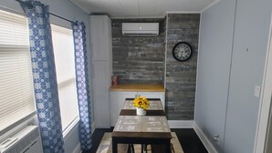 Una cocina compacta con mesa de comedor, sillas, un reloj y un aire acondicionado.