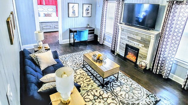 Una sala de estar con sofá, mesa de centro, televisor, chimenea y alfombra estampada.