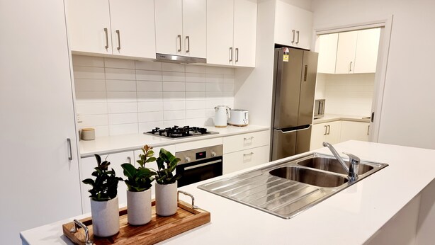 Een moderne keuken met witte kastjes, een roestvrijstalen spoelbak en een houten dienblad met potplanten.