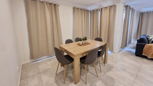 Een eetgedeelte met een houten tafel en zes stoelen, beige gordijnen en een betegelde vloer.