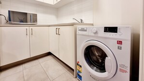 Een kleine wasruimte met een voorlader wasmachine, een magnetron en witte kasten.