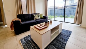 Een woonkamer met een donkerblauwe bank, een salontafel en een grote schuifdeur die uitkomt op een achtertuin.