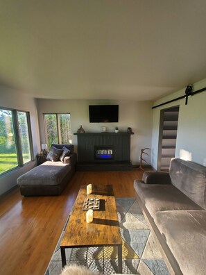 Een moderne woonkamer met een open haard, een bank, een salontafel en een aan de muur bevestigde televisie.
