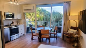 Eine moderne Küche mit Einbauofen, Mikrowelle und Wasserkocher auf der Arbeitsfläche. Es gibt einen Essbereich mit rundem Tisch und Stühlen, sowie einen Balkon mit Blick auf Grünflächen.