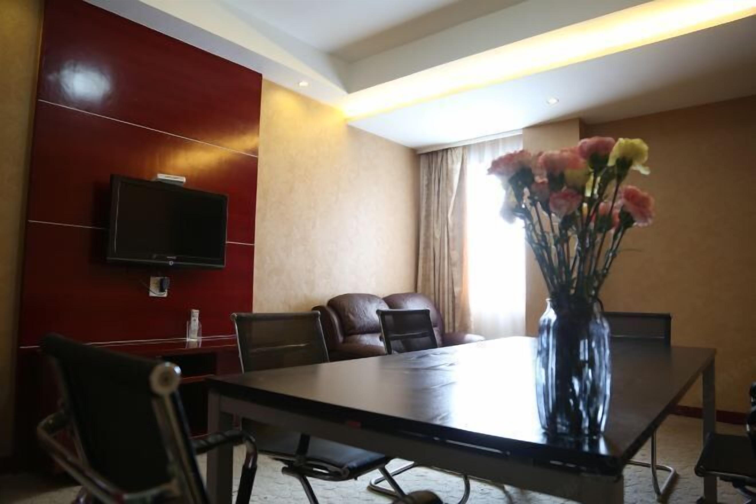 Un salón de conferencias de hotel con una larga mesa, varias sillas, un televisor de pantalla plana montado en la pared y un jarrón con flores sobre la mesa.