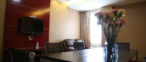 Un salón de conferencias de hotel con una larga mesa, varias sillas, un televisor de pantalla plana montado en la pared y un jarrón con flores sobre la mesa.