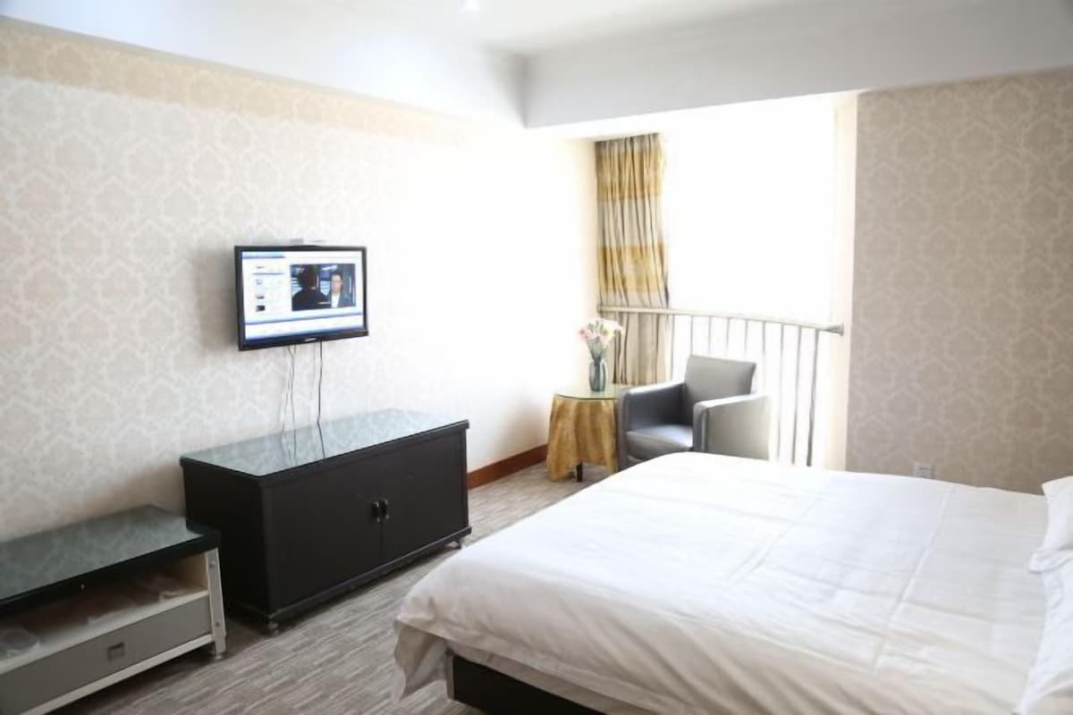 Habitació d'hotel amb un llit, una televisió penjada a la paret, una taula petita amb un vas i una cadira.