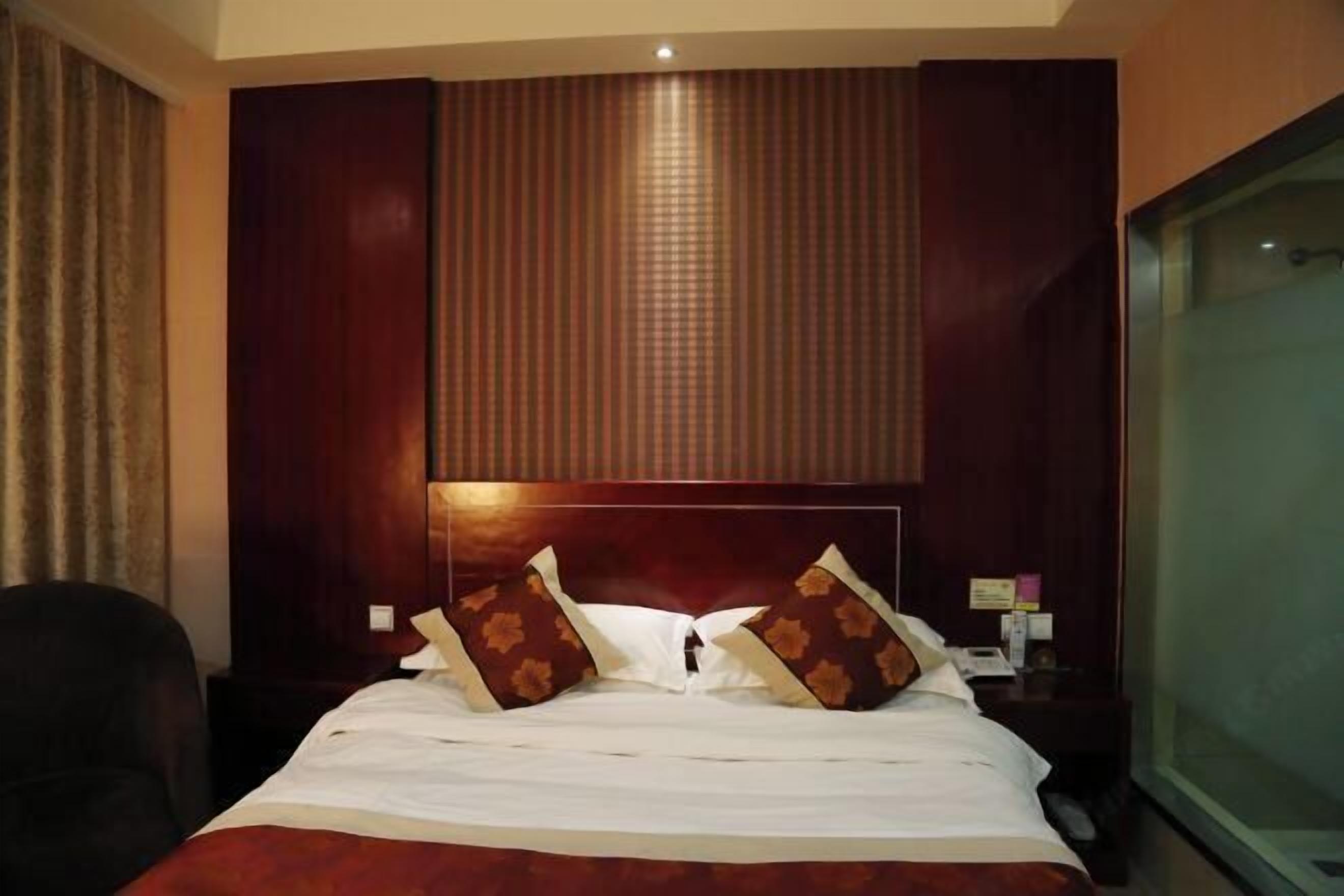 A hotel room with a large bed, a headboard with vertical stripes, a nightstand with a lamp, and a window with curtains.
