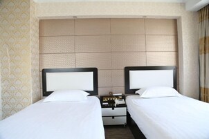 A hotel room with two beds, a nightstand, and a headboard with a textured design.