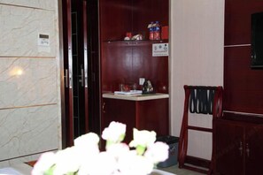 Camera d'albergo con parete in marmo, un armadietto in legno, un piccolo ripiano con articoli da toilette e una sedia.