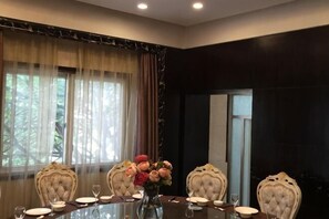 Un salón de conferencias con una mesa de vidrio, cuatro sillas tapizadas, un jarrón con flores y vistas a árboles a través de amplias ventanas.