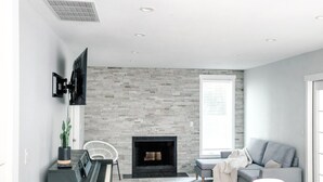 Ein modernes Wohnzimmer mit Kamin aus Stein, einem Klavier, einem grauen Sofa und einem weißen Couchtisch.