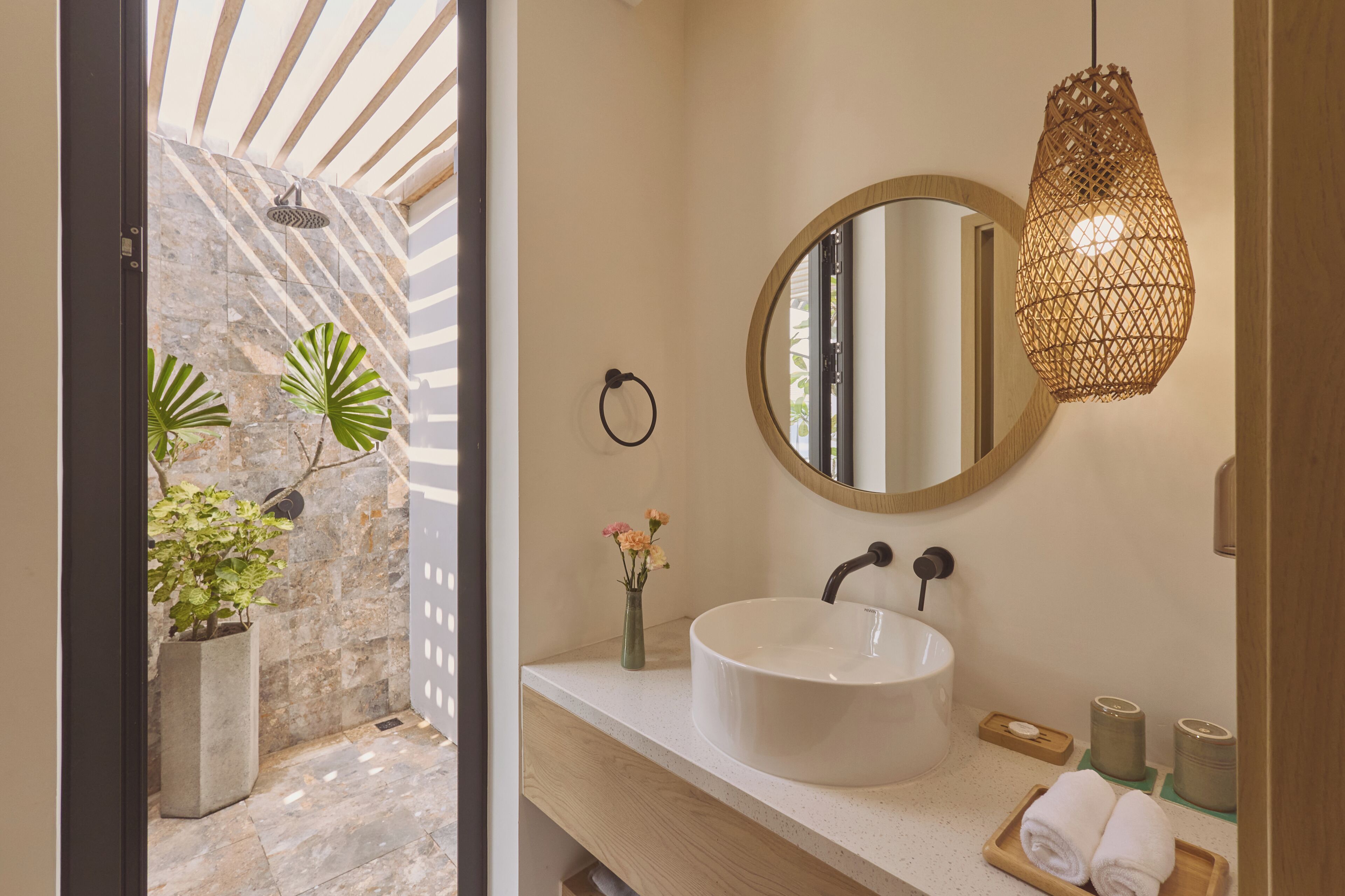 A bathroom with a stone wall, a round mirror, a white sink, a hanging light fixture, and a small potted plant.