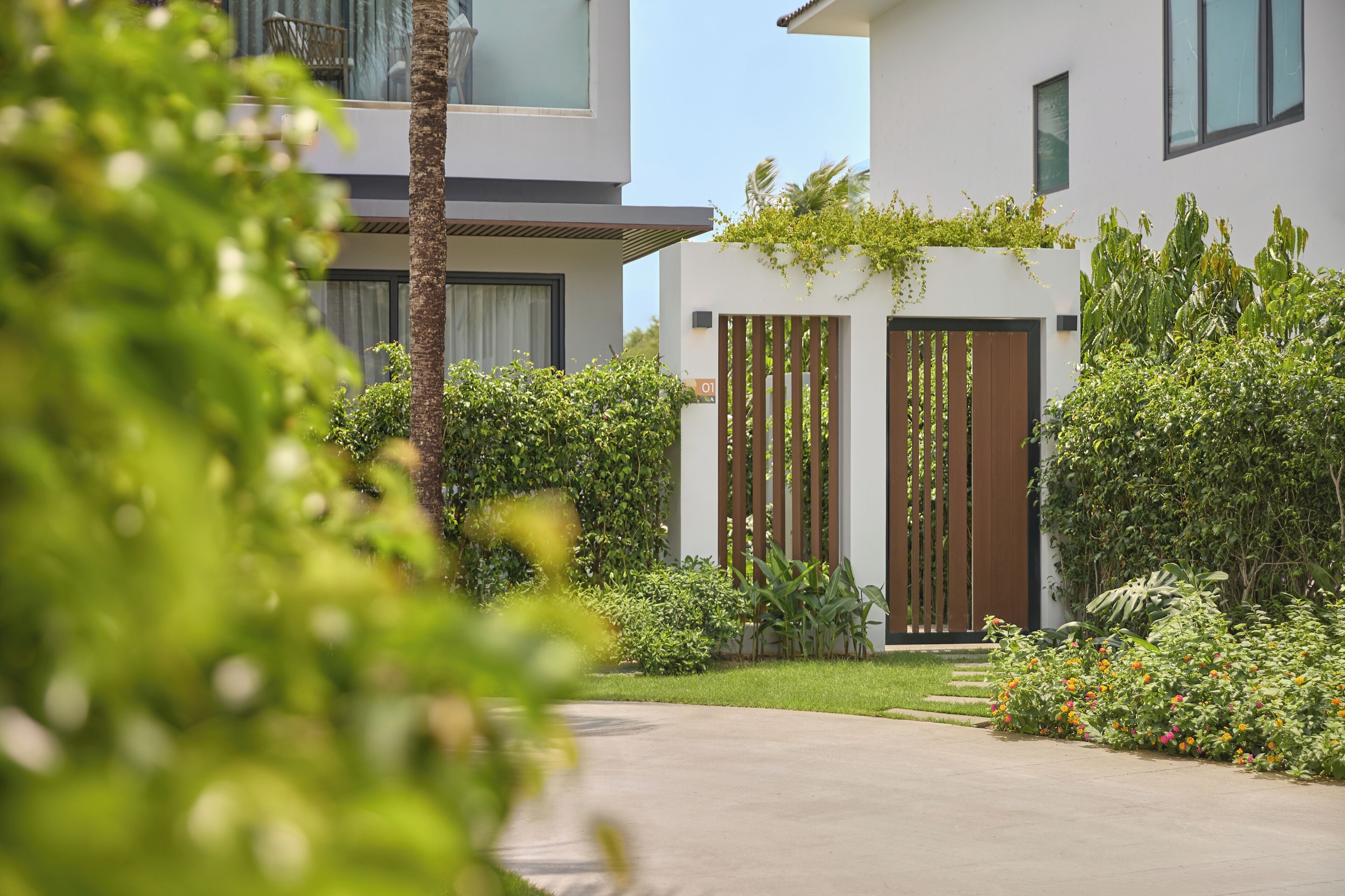 A modern building with a gated entrance, lush greenery, and a clear sky.