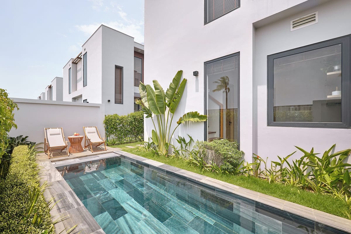 A modern pool area with a clear pool, two lounge chairs, and lush greenery.