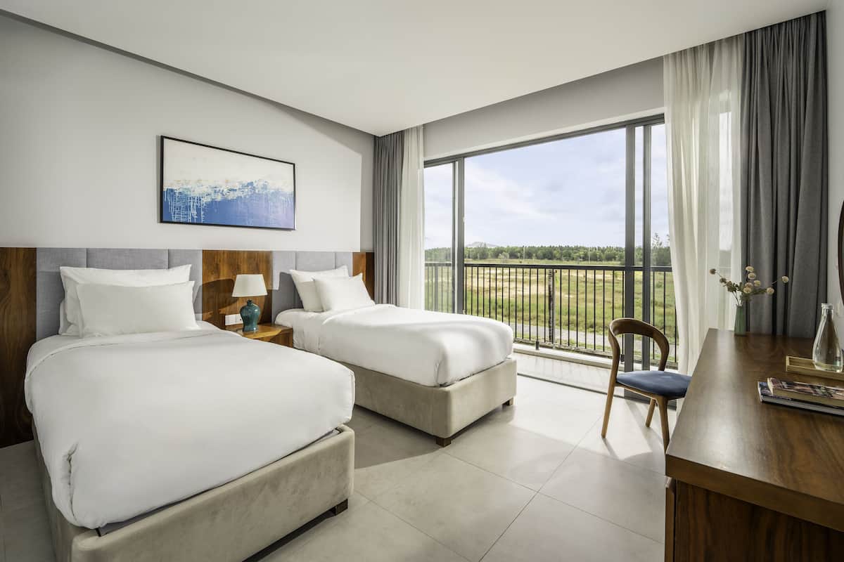 A hotel room with two beds, a desk, and a large window with a view of a green landscape.