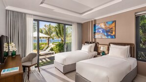 A hotel room with two beds, a desk, a chair, and a large window with a view of palm trees and a pool. - Andochine Resort & Spa Phu Quoc (Phu Quoc)