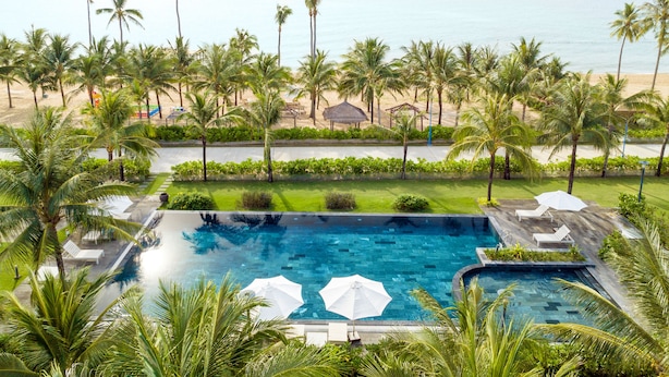 A swimming pool with lounge chairs and umbrellas, surrounded by palm trees and a view of the beach. - Andochine Resort & Spa Phu Quoc (Phu Quoc)
