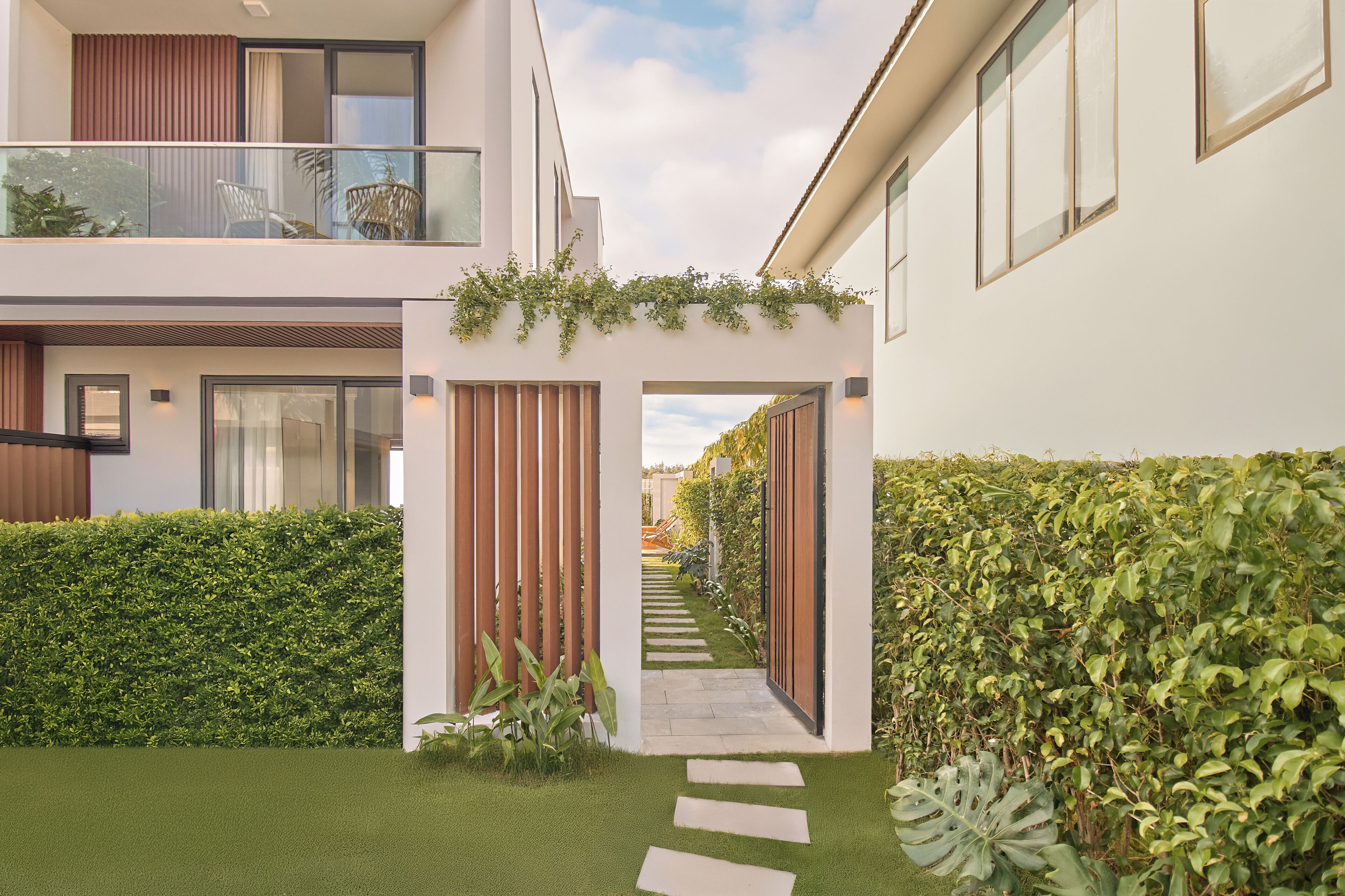 A modern residential building with a glass balcony, a pathway leading to the entrance, and a well-maintained garden.