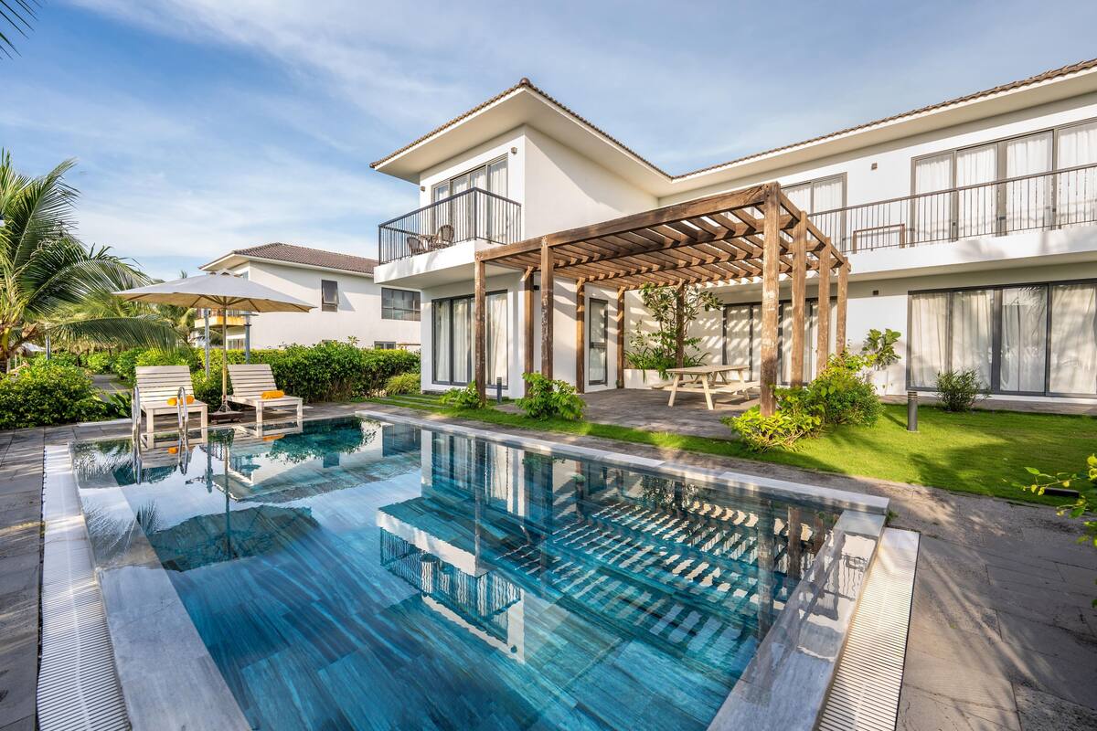 A modern hotel with a swimming pool, outdoor seating, and a covered patio area.