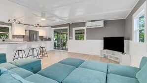Un salon moderne doté d’un grand canapé de couleur turquoise, d’un téléviseur à écran plat et d  ’un coin cuisine avec des meubles blancs et un réfrigérateur en acier inoxydable.