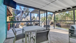Une terrasse couverte avec une table et des chaises, de grandes fenêtres et une vue sur le jardin arrière.