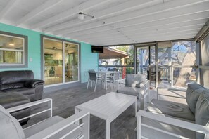 Uma área de estar coberta ao ar livre, com design moderno, com um sofá, cadeiras e uma mesa.
