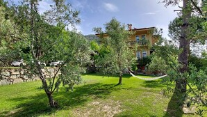 A lush garden with a hammock, a stone wall, and a large building in the background. - Malikane Luxury Resort (Edremit)