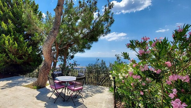 An outdoor seating area with a table and chairs, surrounded by trees and flowering plants, overlooking a scenic view. - Malikane Luxury Resort (Edremit)