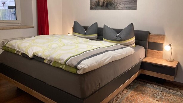 Une chambre moderne avec un grand lit, deux tables de chevet, une commode, un tableau au mur et une fenêtre avec des rideaux.