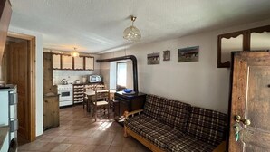 A cozy living room with a plaid sofa, wooden dining table, and a kitchen area with a stove and cabinets. - Mont Blanc, Amazing View From Private Terrace (Cogne)