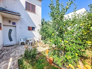 A courtyard with a white building, a tree with green leaves and yellow fruits, and a table with chairs. - Vacation home Ante by Interhome (Brodarica)