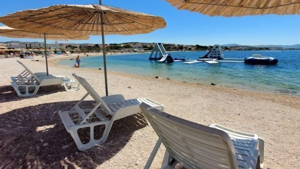 A beach with white plastic lounge chairs and thatched umbrellas, a clear blue sea, and a few boats in the water. - Vacation home Ante by Interhome (Brodarica)