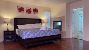 Une chambre à coucher avec un grand lit, deux tables de chevet, une commode, une cheminée et une porte donnant sur une autre pièce.