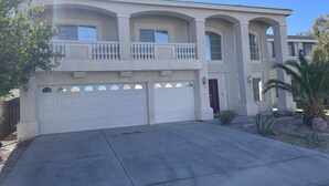 Une maison à deux étages avec un garage, une porte rouge et un balcon.