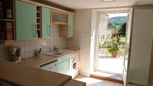 Une cuisine équipée d’un lave-linge, d’une machine à café et offrant une vue sur un jardin grâce à une porte ouverte.
