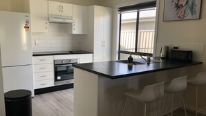 A modern kitchen with white cabinets, a built-in oven, a black countertop, and a window with a view.