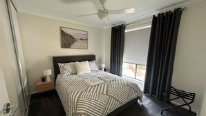 A neatly made bed with striped bedding, a ceiling fan, a nightstand with a lamp, and a window with curtains.